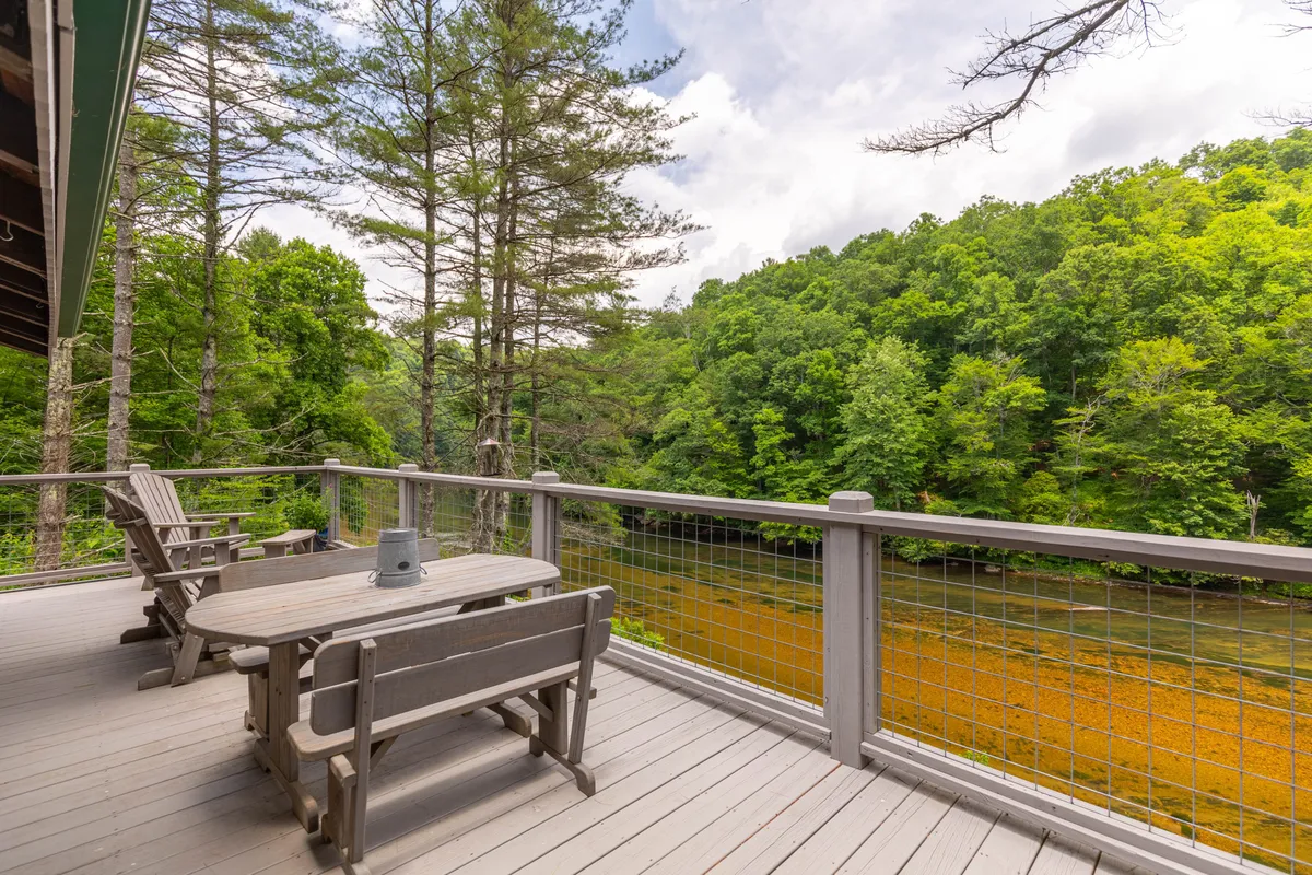 A peaceful exterior deck overlooking a scenic river, surrounded by mature trees and furnished with comfortable outdoor seating. The space is ideal for relaxing outside, watching sunsets, or stargazing beside nature’s beauty.