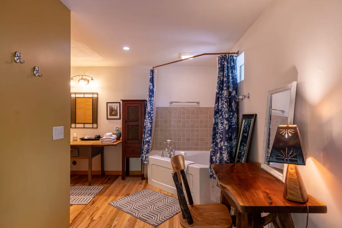 A calming bathroom scene featuring a bathtub perfect for soaking, a desk with a warm lamp for reflection or quiet work, and decorative curtains that bring in gentle natural light. The room is styled to feel intimate and relaxing.