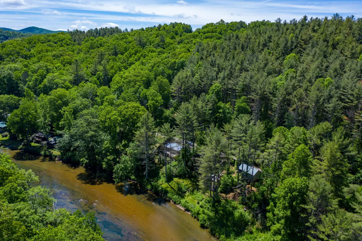 A picturesque view of the river bordered by dense greenery, with cozy cabins nestled nearby. The scene radiates peace and rejuvenation, perfect for fishing, hiking, or gathering around a campfire as the sun sets.