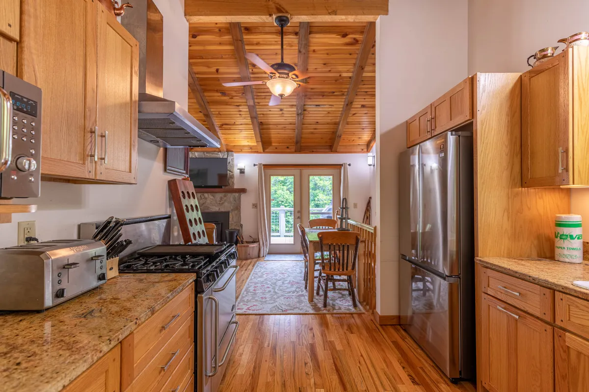 An open-concept space combining a kitchen, dining table, and living area. Wooden beams and large windows create a bright, airy atmosphere, while the kitchen island and dining table offer plenty of space for meals and entertaining.