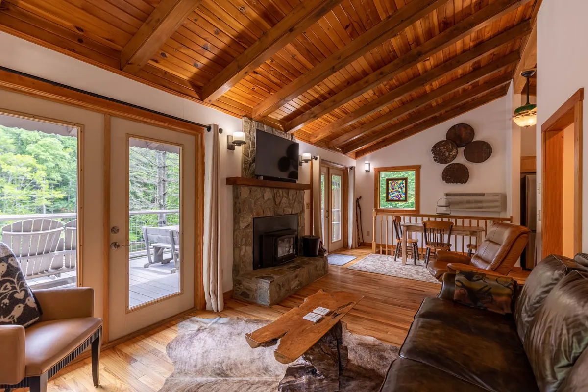 A welcoming interior living space with a prominent fireplace, exposed wooden beams, large windows that draw in nature views, and comfortable seating. The entry area is visible, suggesting easy access from outside and a practical spot for transitioning from adventure to relaxation.
