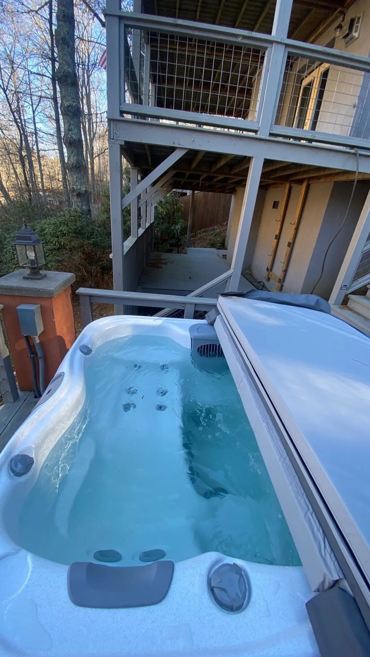 A view of the spacious deck with a hot tub surrounded by nature, emphasizing privacy and serenity. The hot tub is well-positioned for guests to soak under the stars or enjoy the scenic foliage during the day.